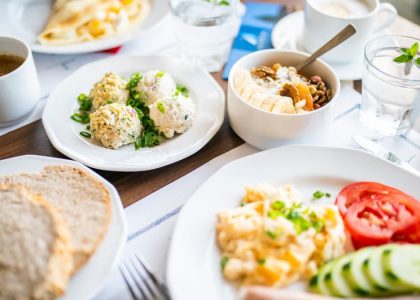 From above of tasty brunch of power bowl and scrambled eggs with fresh vegetable slices against drinks on table