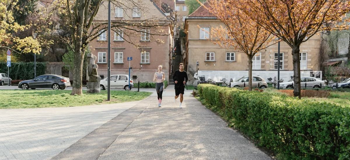 A couple jogging together in an urban park surrounded by greenery and houses.