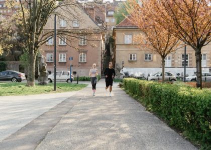 A couple jogging together in an urban park surrounded by greenery and houses.