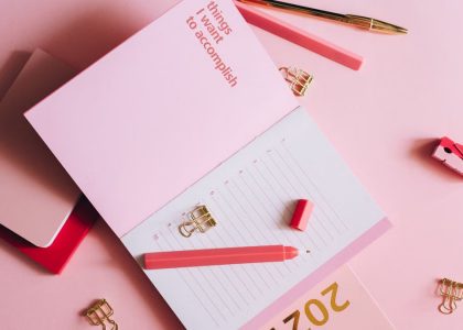 Organized workspace with pink planner, pen, and clips on pastel background.